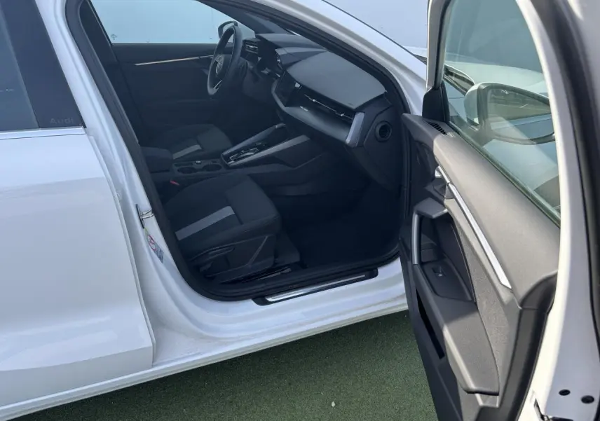 Intérieur côté conducteur d'une Audi A3 Sportback blanche, montrant sièges noirs et tableau de bord moderne.