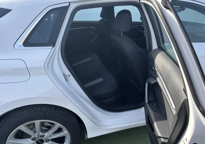 Vue côté gauche arrière d'une Audi A3 Sportback 2024 blanc Arkona avec porte arrière ouverte et intérieur noir visible.