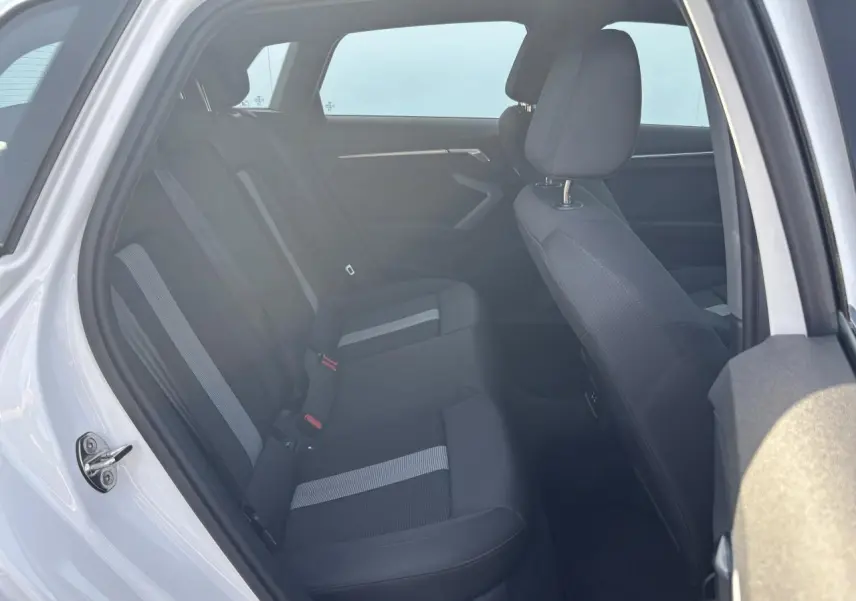 Vue intérieure côté gauche de l'Audi A3 Sportback 2024 en Blanc Arkona, sièges tissu noir avec bandes grises.