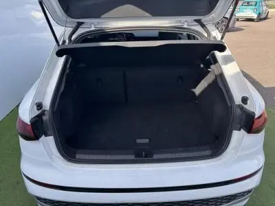 Coffre ouvert vu de l'arrière d'une Audi A3 Sportback 2024 en blanc Arkona, intérieur noir spacieux et propre.