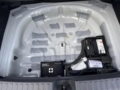Coffre ouvert d'une Audi A3 Sportback blanc Arkona montrant le rangement sous plancher avec kit de réparation et trousse de secours.