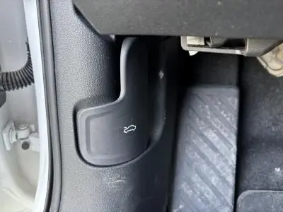 Gros plan sur le levier d'ouverture du coffre côté conducteur d'une Audi A3 Sportback blanche 2024.