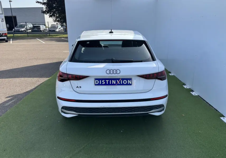 Vue arrière d'une Audi A3 blanche Arkona avec feux arrière LED et logo distinctif sur fond vert.