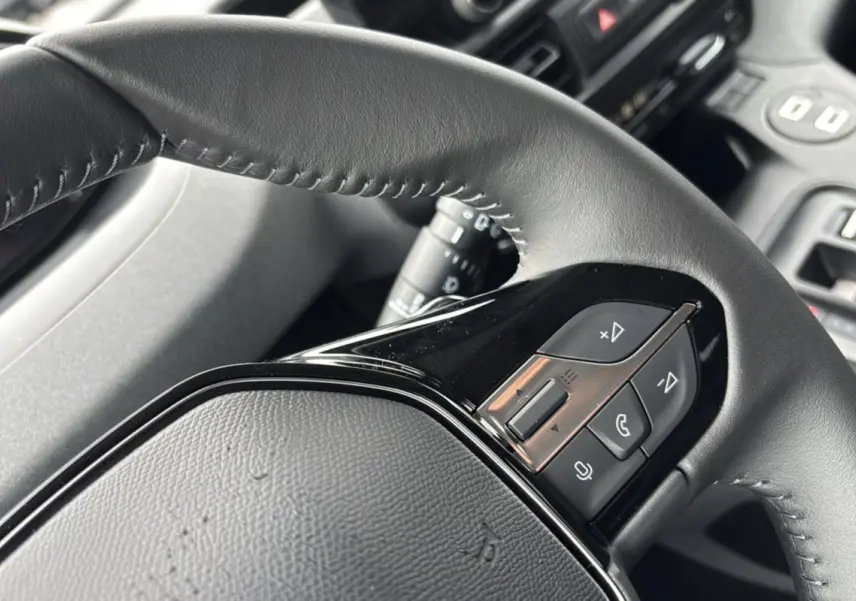 Gros plan sur le volant cuir multifonctions noir du Peugeot Rifter, avec commandes audio et téléphone intégrées.