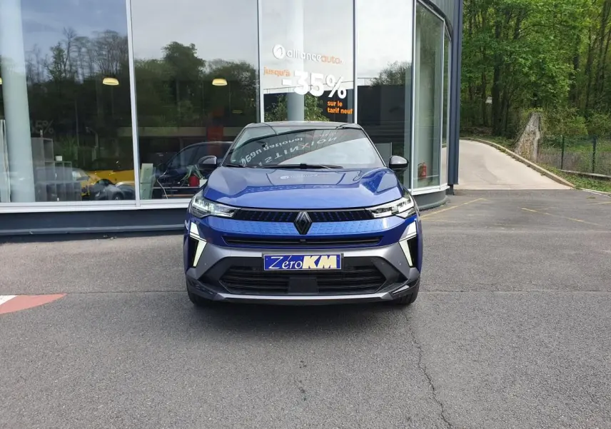 Vue avant d'un Renault Captur bleu Iron 2026 avec calandre moderne et éclairage LED distinctif, stationné devant un showroom.