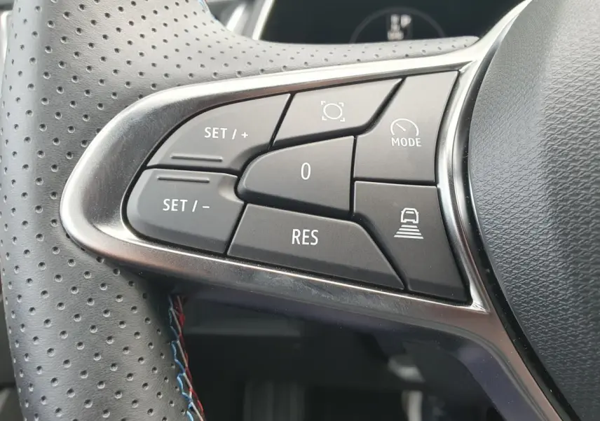 Gros plan sur les commandes au volant du Renault Captur 2026, boutons noirs avec surpiqûres tricolores sur cuir perforé.