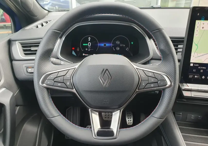 Vue rapprochée du volant noir perforé avec surpiqûres tricolores du Renault Captur 2026, tableau de bord numérique et écran tactile visible.