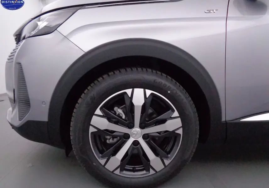 Gros plan sur la roue avant gauche du Peugeot 3008 gris Artense Métal avec badge GT visible sur l'aile.