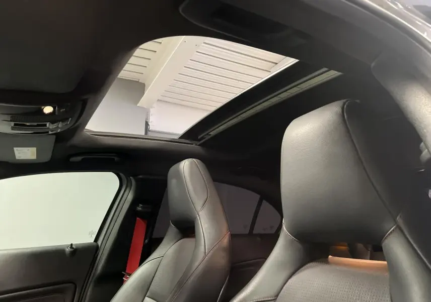 Intérieur de la Mercedes Classe A 45 AMG 2015, vue des sièges sport noirs avec surpiqûres rouges et toit ouvrant panoramique.