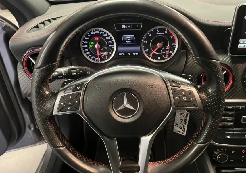 Vue rapprochée du volant sport noir à surpiqûres rouges de la Mercedes Classe A 45 AMG, tableau de bord et compteurs visibles.