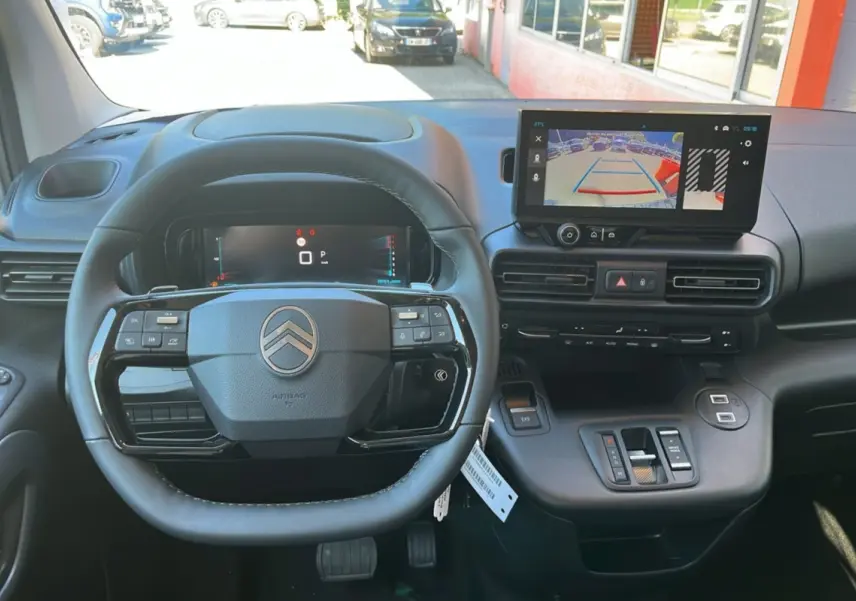 Vue intérieure frontale du tableau de bord et volant cuir noir du Citroën Berlingo 2026 avec écran tactile et caméra de recul affichée.