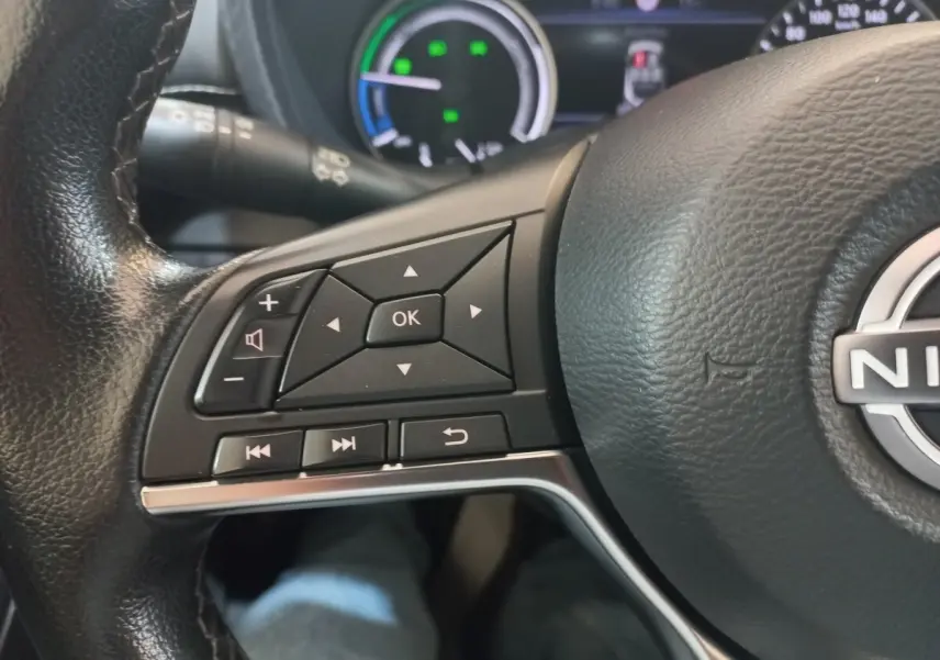 Gros plan sur le volant cuir et alu du Nissan Juke Hybrid 143 Business+ 2023, avec commandes multifonctions visibles.
