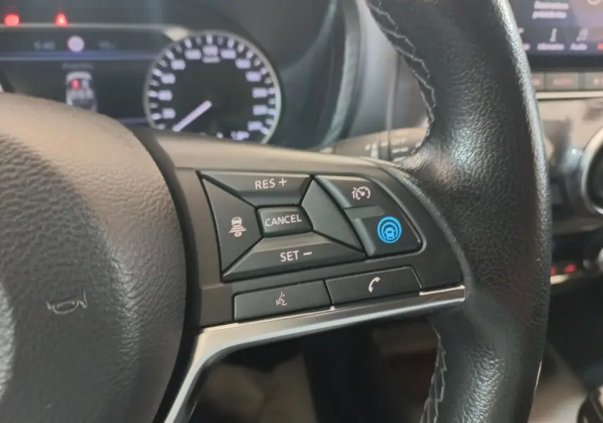 Gros plan sur le volant cuir et alu côté gauche du Nissan Juke Hybrid 143 Business+ 2023 avec commandes multifonctions.