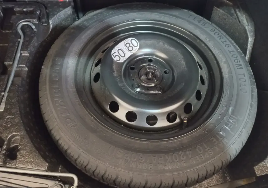 Gros plan sur la roue de secours noire dans le coffre du Nissan Juke Hybrid 143 Business+ gris foncé.
