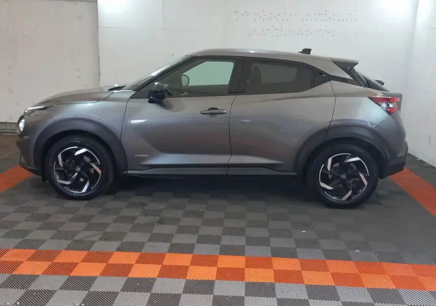 Vue de profil côté gauche du Nissan Juke Hybrid 143 Business+ gris foncé avec jantes noires et détails noirs contrastants.