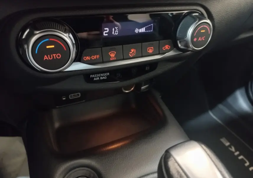 Gros plan sur la console centrale du Nissan Juke Hybrid 143 Business+ 2023, avec commandes climatisation et affichage digital.