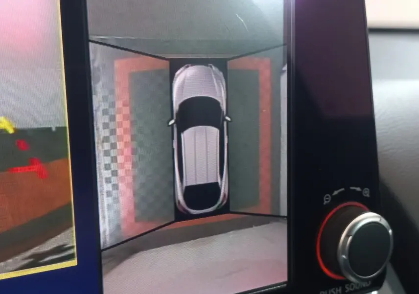 Vue écran intérieur montrant la caméra 360° du Nissan Juke Hybrid 143 Business+ gris foncé en vue aérienne.
