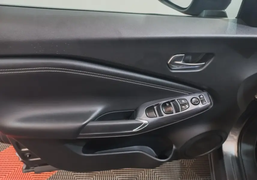 Vue intérieure du panneau de porte côté conducteur du Nissan Juke Hybrid 143 Business+ gris foncé, avec commandes électriques et surpiqûres blanches.