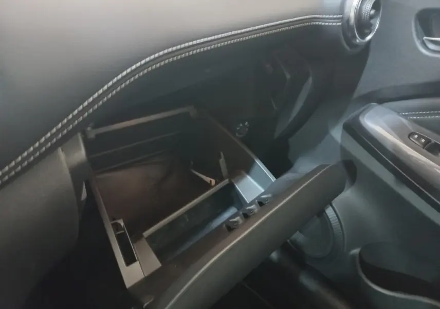 Intérieur du Nissan Juke Hybrid 2023, vue sur la boîte à gants ouverte avec surpiqûres blanches sur tableau de bord noir.