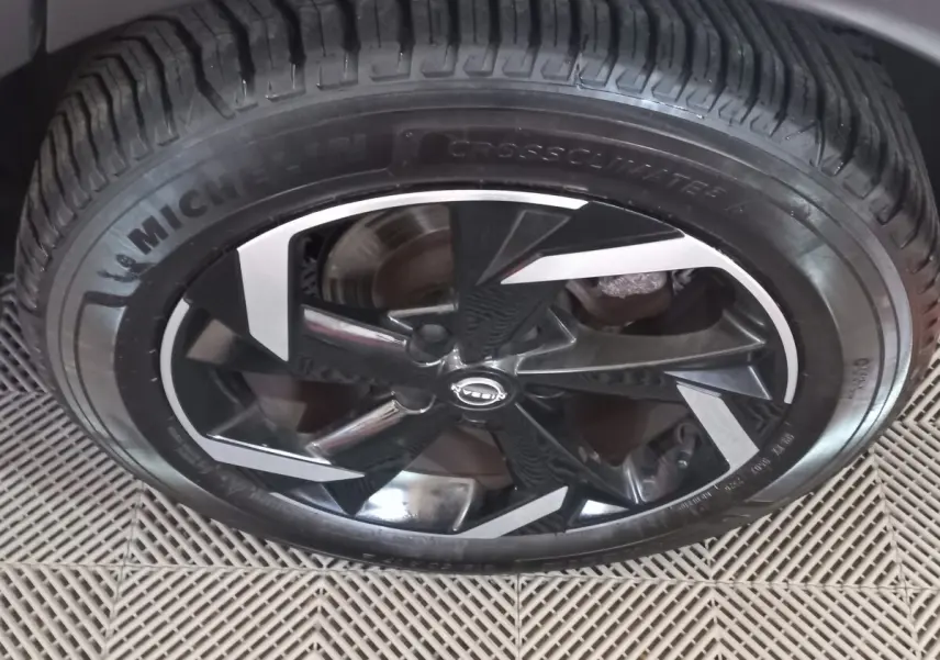 Gros plan sur la jante noire et argentée du Nissan Juke Hybrid 143 Business+ gris foncé, avec pneu Michelin CrossClimate.