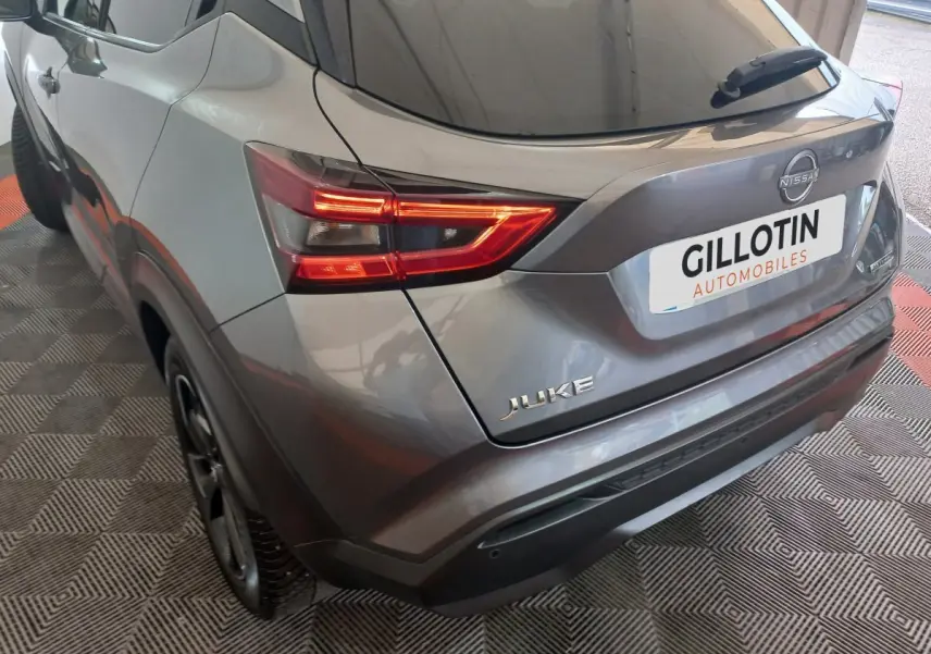 Vue 3/4 arrière droite du Nissan Juke Hybrid gris foncé avec feux LED allumés et logo visible sur hayon.