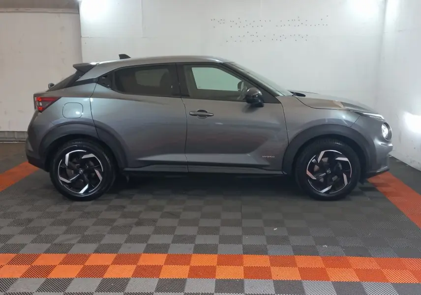 Vue profil droit du Nissan Juke Hybrid 143 Business+ gris foncé avec jantes noires et détails hybrides visibles.