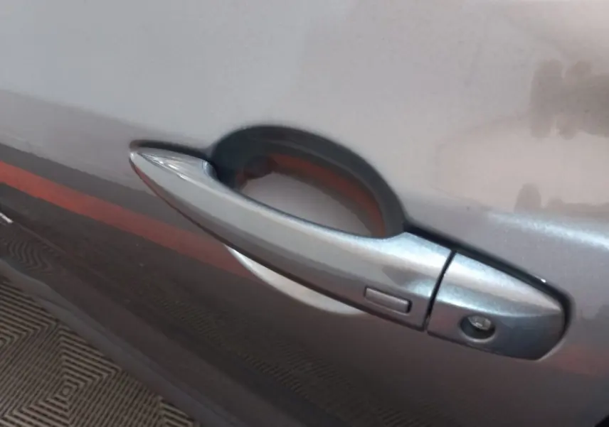 Poignée de porte côté gauche gris foncé du Nissan Juke Hybrid 143 Business+ 2023, avec bouton de déverrouillage intégré.
