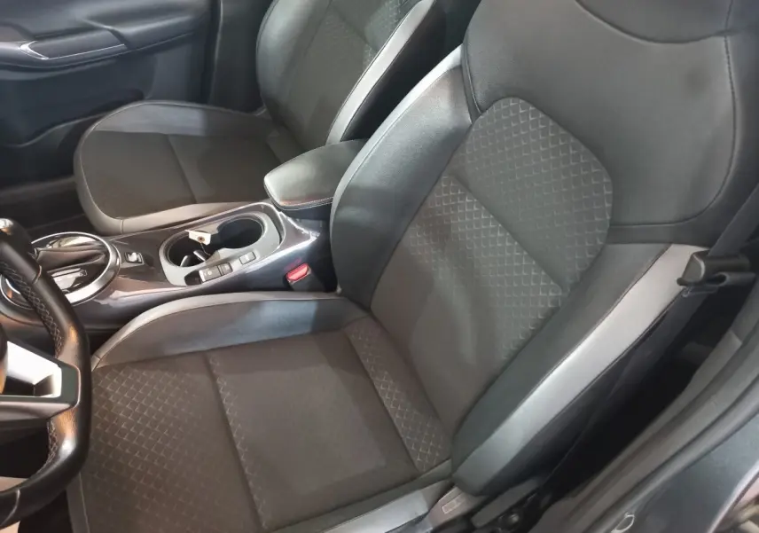 Vue intérieure côté conducteur du Nissan Juke Hybrid 143 Business+ 2023, sièges tissu gris avec accoudoir central cuir.