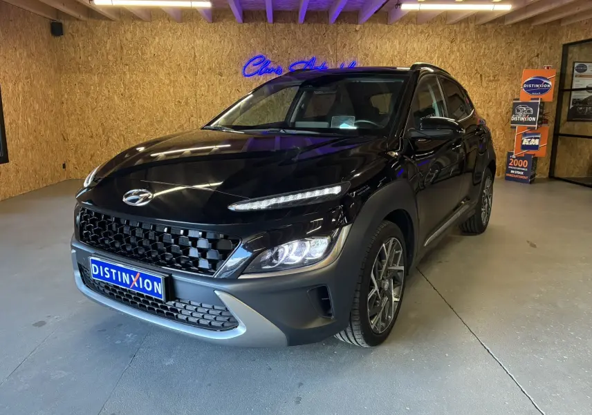 Vue 3/4 avant d'un Hyundai Kona noir 2023 avec calandre noire et phares LED allumés en intérieur showroom.
