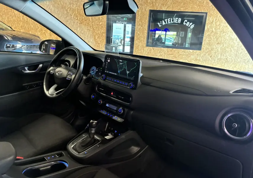 Intérieur noir du Hyundai Kona 2023, vue côté conducteur montrant volant, écran tactile et console centrale avec boîte auto.