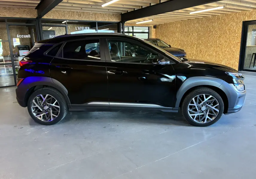 Profil côté gauche d'un Hyundai Kona noir 2023 en version 1.6 GDI 140 Creative, avec jantes alliage et protections plastiques grises.