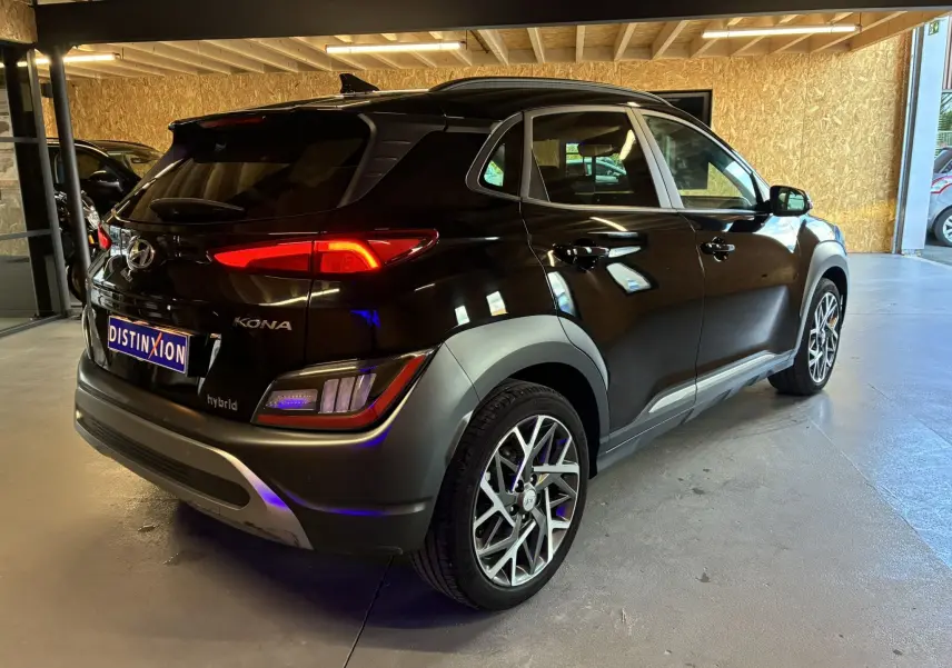 Vue 3/4 arrière droite d'un Hyundai Kona noir hybride 2023 avec jantes alliage et feux arrière LED allumés.