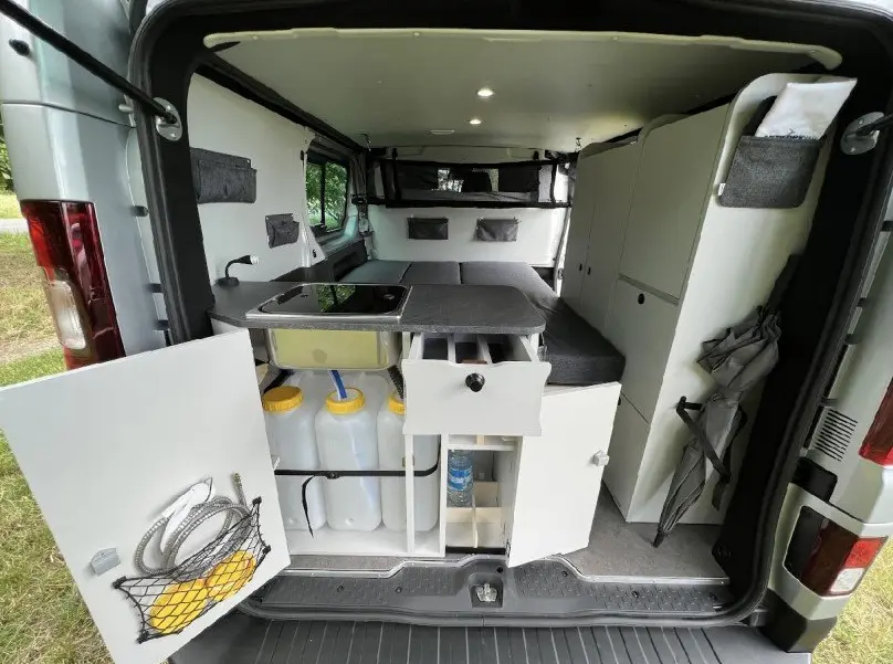Vue arrière intérieure du Renault Trafic Fourgon gris 2025 aménagé avec kitchenette, rangements et couchage.