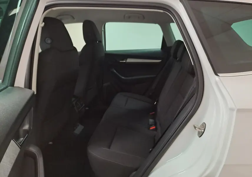 Vue côté gauche arrière sur l’intérieur du Skoda Karoq blanc Lune, montrant les sièges arrière noirs et la porte ouverte.