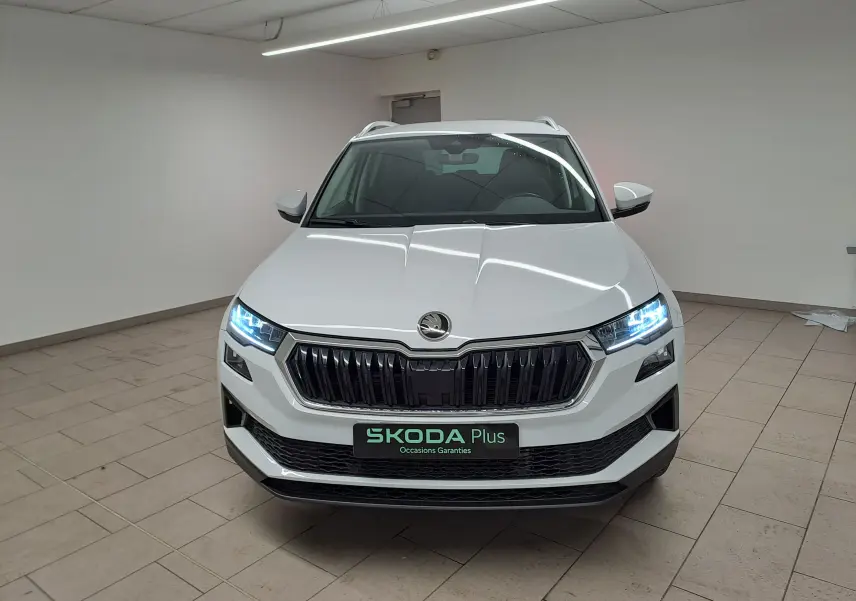 Vue avant d’un Skoda Karoq blanc Lune 2025 avec calandre noire, phares allumés et pack chrome extérieur visible.
