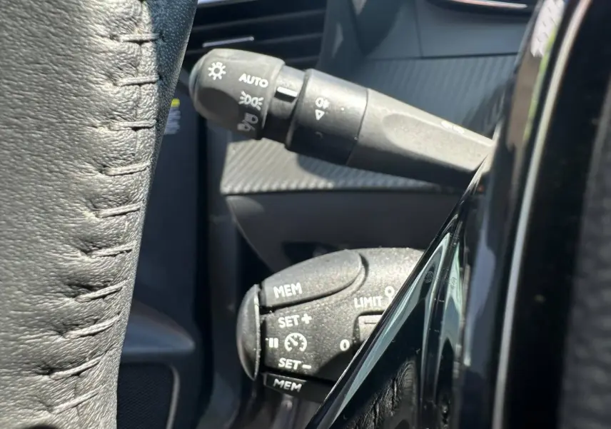 Gros plan sur les commandes au volant de la Peugeot 208 1.2 100ch Allure, avec détails en noir mat et cuir noir.