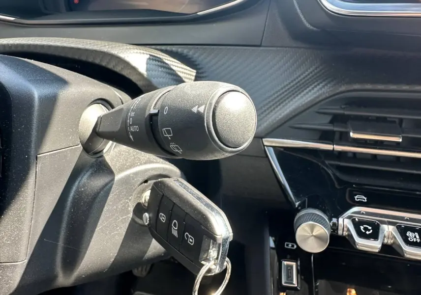 Gros plan intérieur sur la colonne de direction et la clé insérée d'une Peugeot 208 gris Selenium, avec tableau de bord noir brillant.