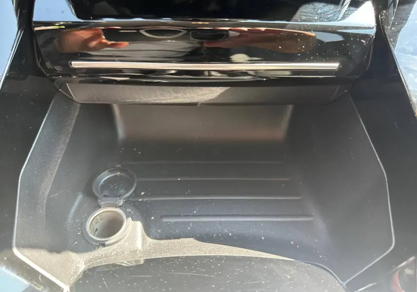 Vue rapprochée de la prise 12V ouverte dans le rangement central avant d'une Peugeot 208 gris Selenium.