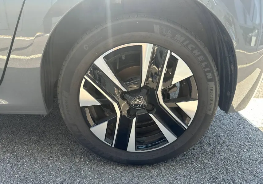 Gros plan sur la jante alu bicolore noire et argentée du côté avant droit d'une Peugeot 208 gris Selenium.