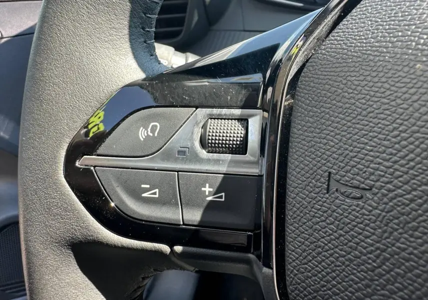 Gros plan sur les commandes noires du volant côté gauche de la Peugeot 208 1.2 100ch Gris Selenium 2025.