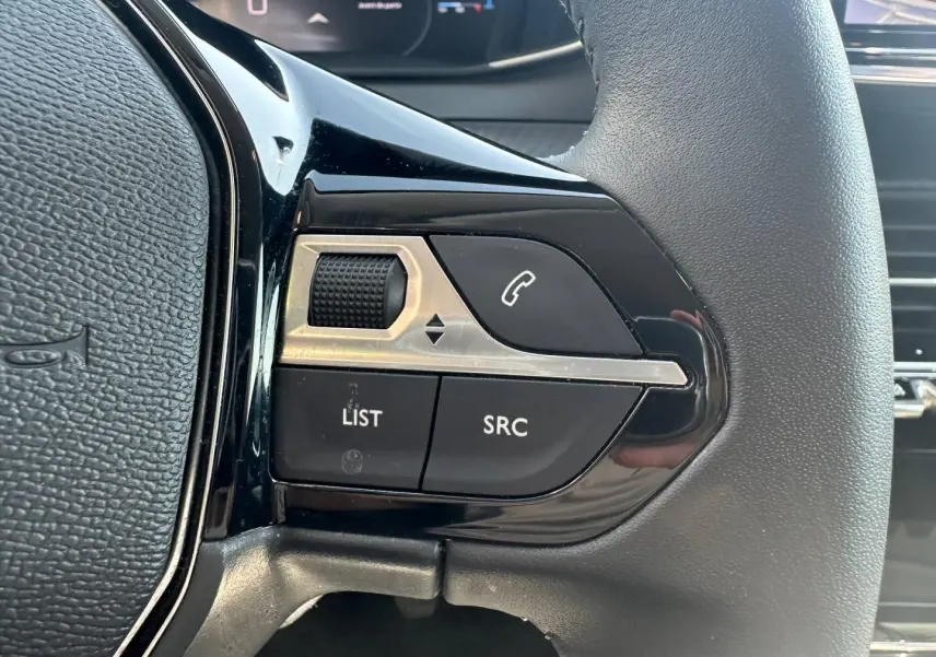Gros plan sur les commandes gauche du volant noir de la Peugeot 208 2025, boutons SRC, LIST et molette de réglage.
