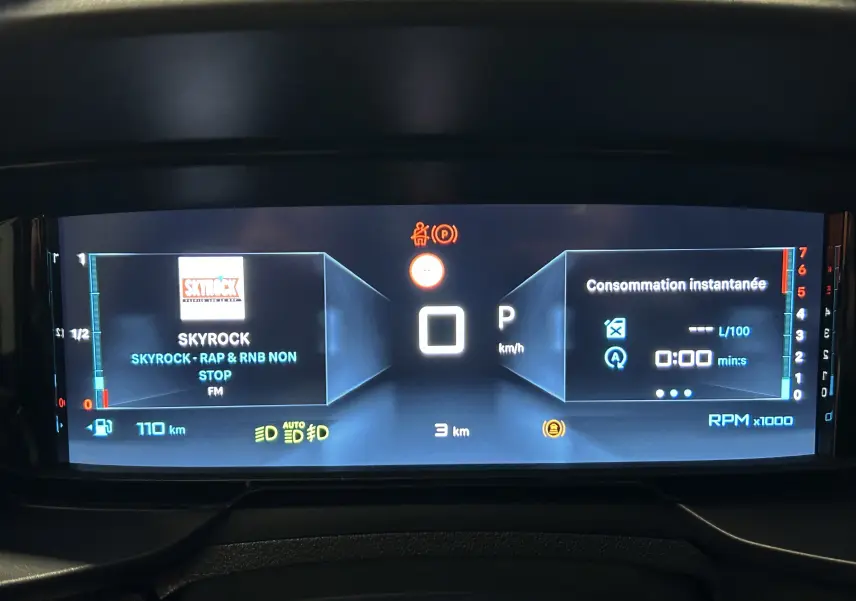 Affichage numérique du tableau de bord du Citroën Berlingo gris, montrant la radio Skyrock et la consommation instantanée.