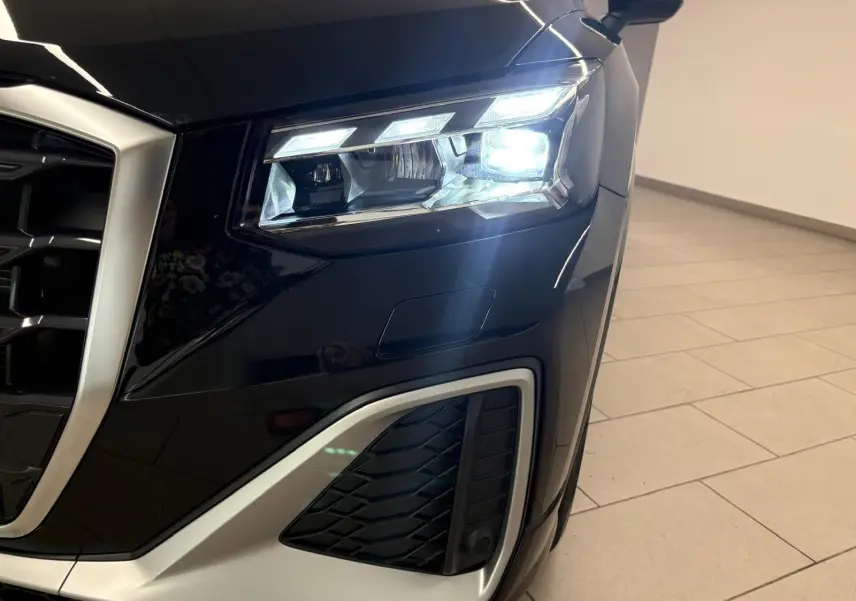 Gros plan sur le phare avant droit allumé d’un Audi Q2 35 TFSI S Line noir mythic, avec calandre et partie basse argentées.