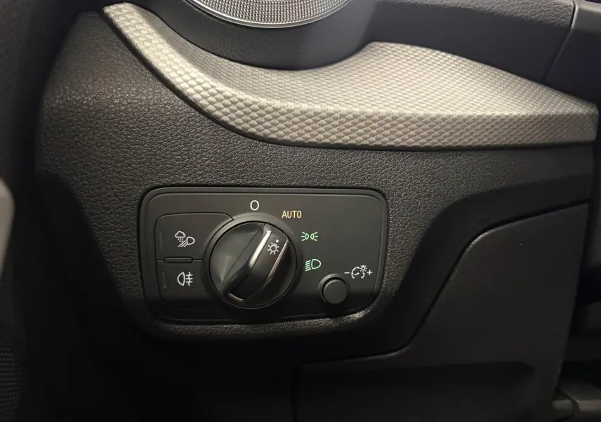 Gros plan sur le panneau de commande des phares à gauche du volant dans l’Audi Q2 35 TFSI S Line noir Mythic.