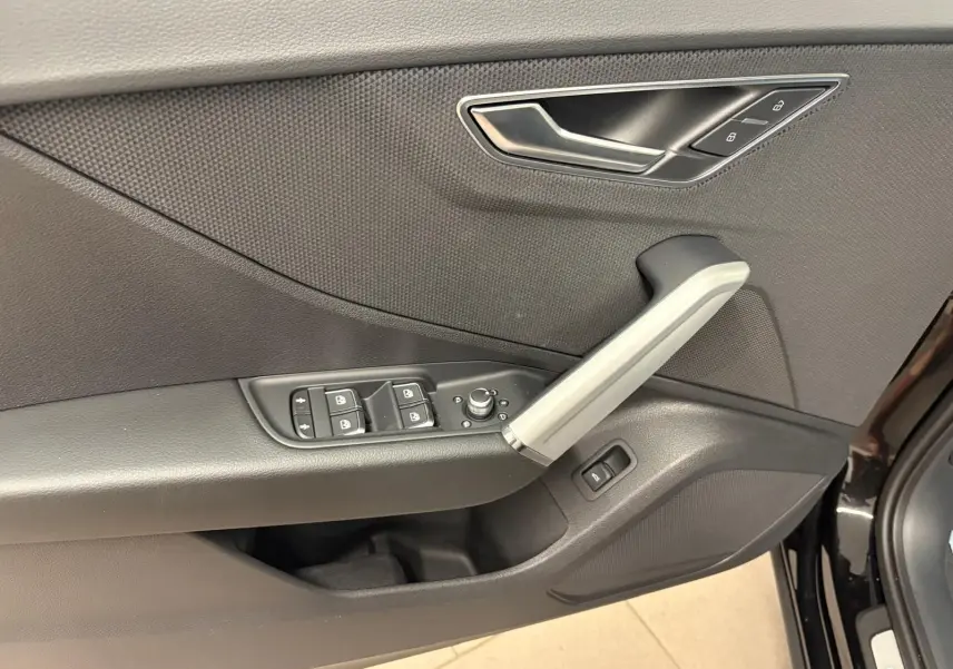 Gros plan sur la porte avant gauche de l'Audi Q2 Noir Mythic, montrant les commandes des vitres et la poignée intérieure grise.