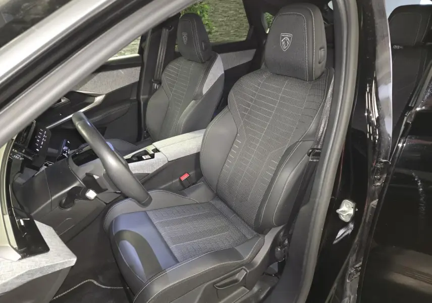 Vue intérieure côté conducteur du Peugeot 3008 Hybrid 2025 noir, sièges tissu et cuir avec logo Peugeot brodé.