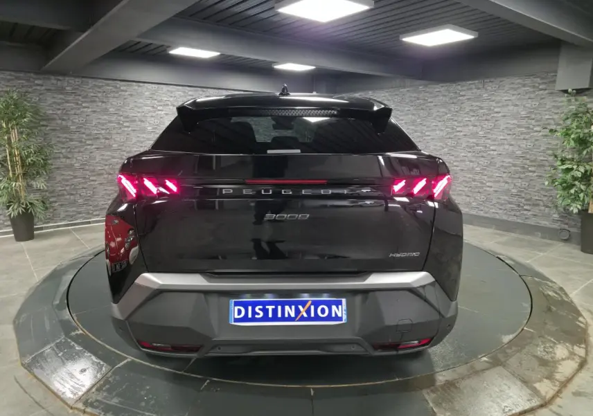 Vue arrière d'un Peugeot 3008 noir hybride 2025 avec feux arrière à griffes LED allumés dans un showroom.