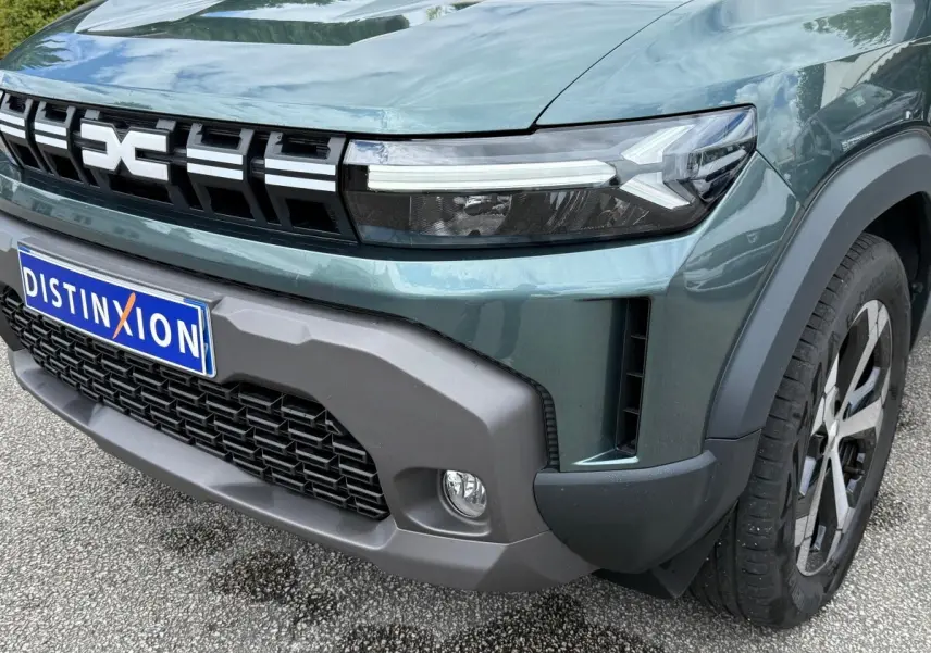 Gros plan sur l’avant droit du Dacia Duster Hybrid 140 Journey vert cèdre, mettant en valeur la calandre et les phares LED.