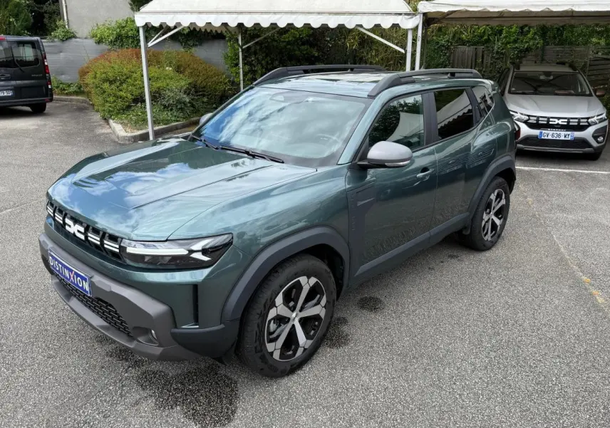 Dacia Duster Hybrid 140 Journey vert cèdre en 3/4 avant droit, avec jantes noires et toit ouvrant visible.