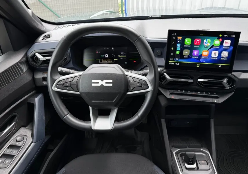 Vue intérieure frontale du tableau de bord du Dacia Duster Hybrid 140 Journey avec écran tactile et volant multifonctions.